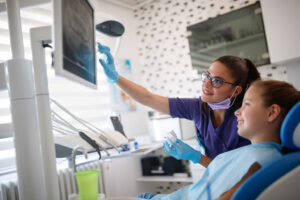 Dentist in dental ordination with female young patient looking at her dental x-ray