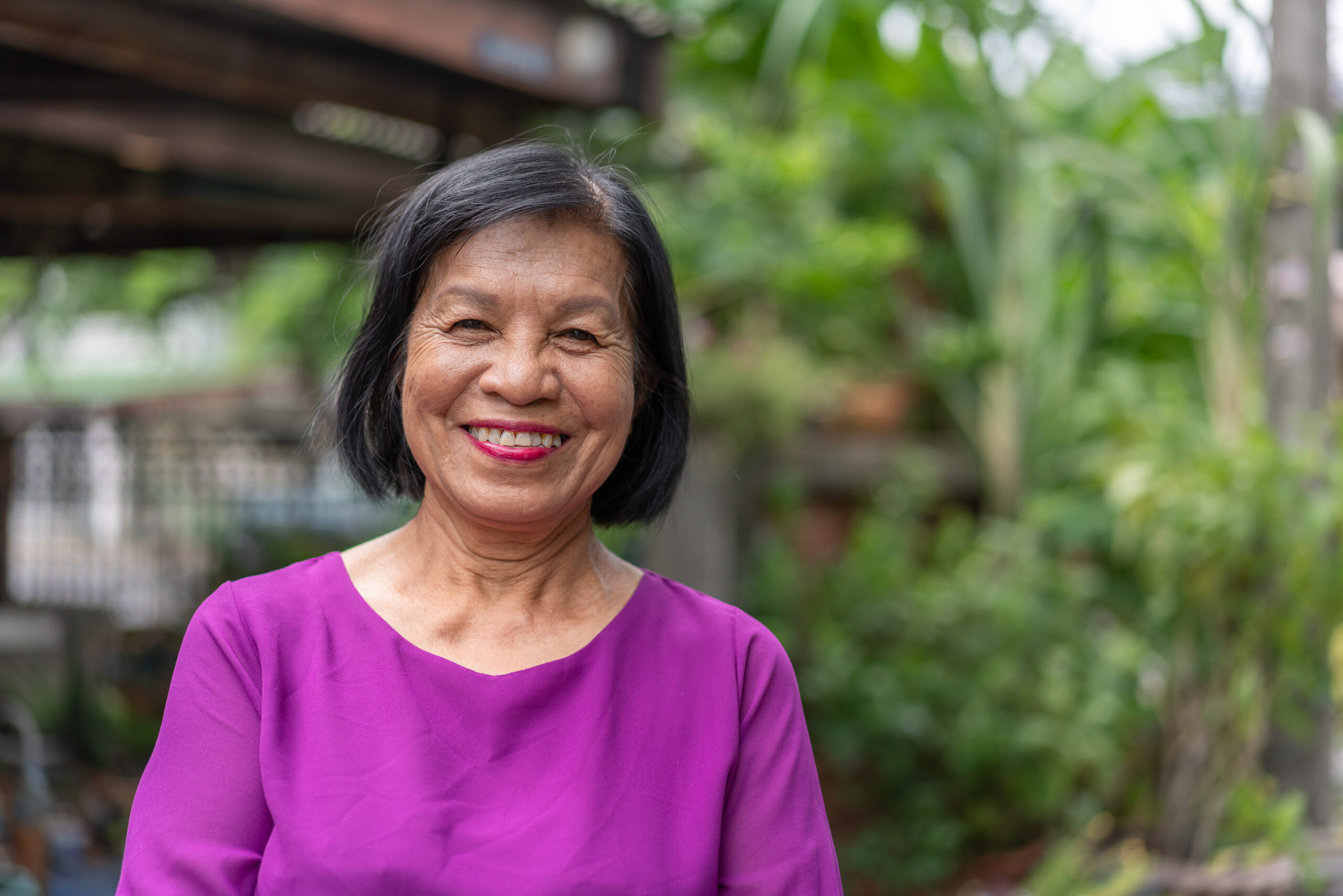 Smiling Asian elderly woman looking at camera standing outside at home