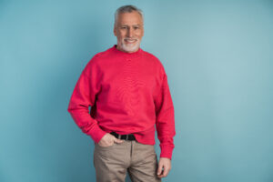 Handsome, mature man in a crimson pullover posing on a blue background. Smiling, confident man standing isolated on a copy space
